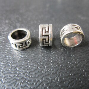 May include: Three silver metal beads with a geometric pattern. The beads are round and have a hole in the center.