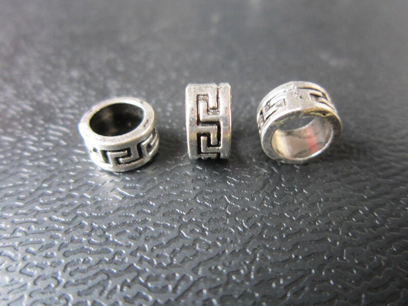 May include: Three silver metal beads with a geometric pattern. The beads are round and have a hole in the center.
