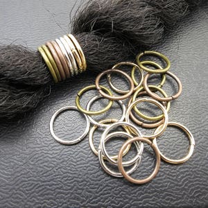 May include: A close-up of a variety of gold, silver, and bronze hair rings. The rings are arranged in a pile on a dark surface.