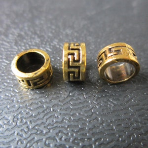 May include: Three gold-colored metal beads with a geometric pattern. The beads are round and have a hole in the center.