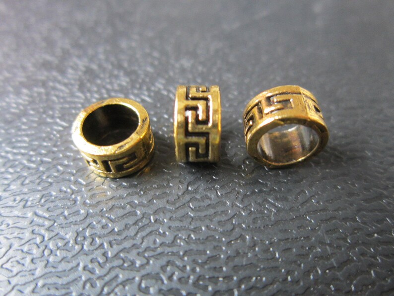 May include: Three gold-colored metal beads with a geometric pattern. The beads are round and have a hole in the center.