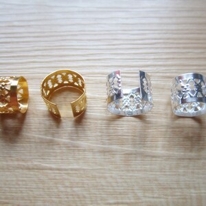 Op de afbeelding: Vier metalen haarre ringen met een decoratief opengewerkt ontwerp. Twee ringen zijn goud en twee zijn zilver.