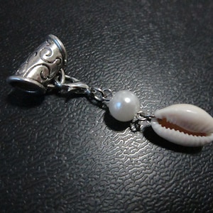 May include: A silver hair tie with a decorative design, a white pearl bead, and a white seashell charm.