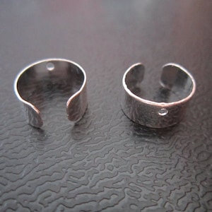 May include: Two silver metal ear cuff rings with a small hole on the top of each ring.