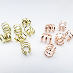 Op de afbeelding: Een set van 12 oormanchetten in twee kleuren: goud en roségoud. De oormanchetten zijn gemaakt van metaal en hebben een eenvoudig, elegant ontwerp.