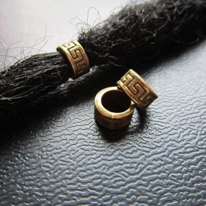 May include: Three gold-colored metal beads with a Greek key design. The beads are for use with dreadlocks.