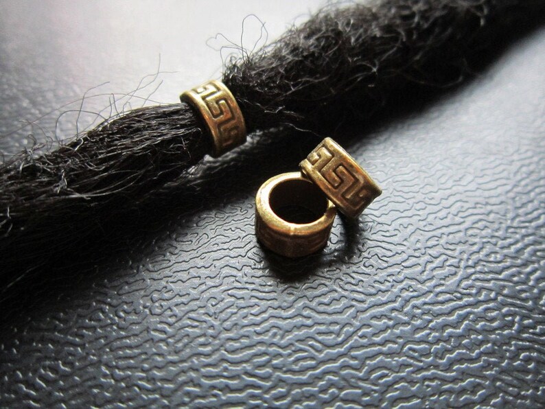 May include: Three gold-colored metal beads with a Greek key design. The beads are for use with dreadlocks.