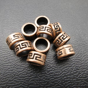 May include: A group of ten copper-colored metal beads with a black Greek key pattern. The beads are round and have a hole in the center.