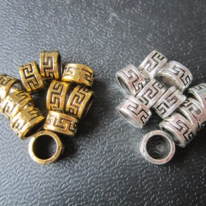 May include: A group of gold and silver metal beads with a Greek key design. The beads are stacked on top of each other and have a shiny finish.
