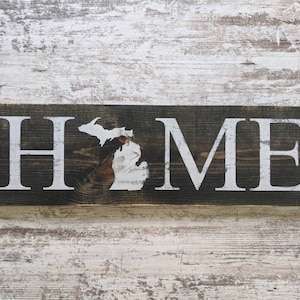 May include: A wooden sign with the word "HOME" in white letters. The letter "O" is replaced with the outline of the state of Michigan.