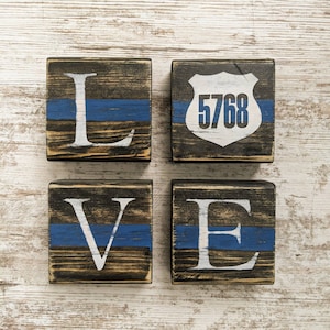 May include: Four wooden blocks spelling out the word "LOVE" with a blue and black police stripe design. The third block features a white police badge with the number "5768" on it.