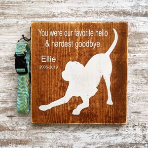 May include: Wooden sign with a white silhouette of a dog, the text "You were our favorite hello & hardest goodbye. Ellie 2006-2019" and a blue and green dog collar.