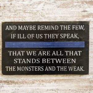 May include: A rectangular wooden sign with a black background and white text. The text reads, "AND MAYBE REMIND THE FEW, IF ILL OF US THEY SPEAK, THAT WE ARE ALL THAT STANDS BETWEEN THE MONSTERS AND THE WEAK." A blue line is across the middle.