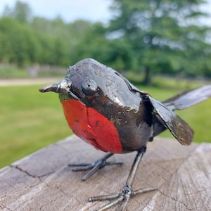 May include: A metal sculpture of a robin, painted black with a red breast. The sculpture is perched on a wooden surface.