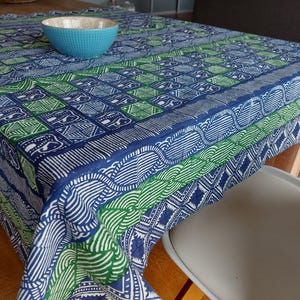Könnte beinhalten: Eine blaue und grüne gemusterte Tischdecke mit einem weißen geometrischen Design. Die Tischdecke ist über einen Holztisch und einen weißen Stuhl gelegt.