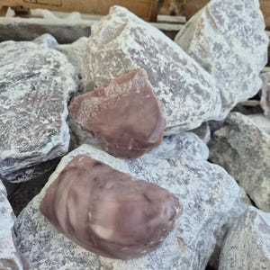 Peut inclure: Une collection de grosses pierres brutes à l'extérieur gris pâle et poussiéreux. Deux pierres centrales présentent des surfaces lisses et polies avec des motifs tourbillonnants dans des tons mauve sourd, vieux rose et blanc crème.
