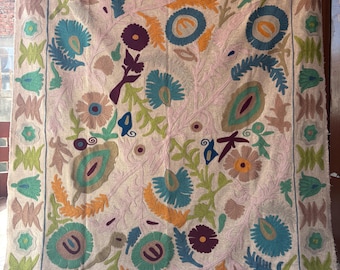 May include: A large, rectangular textile with an intricate floral design. The embroidery features a cream-colored background with vibrant flowers in shades of blue, green, orange, and purple. The border has a repeating geometric pattern.