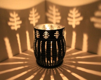 May include: A black metal candle holder with a decorative design of leaves and stripes. The candle holder casts intricate shadows on the surface below.