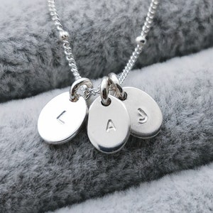 May include: Silver necklace with three oval charms, each engraved with a letter: L, A, and J.