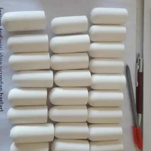 May include: A collection of twenty-four white, cylindrical, rounded-tip objects arranged in three vertical columns. A dark-colored pen with a red cap is positioned to the right of the objects for scale, showing the items are approximately 1.5 inches long.
