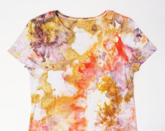 May include: A tie-dye t-shirt with a white background and a colorful pattern of orange, yellow, pink, and purple.