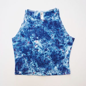 May include: A blue and white tie-dye crop top with red speckles. The top has a scoop neck and a relaxed fit.
