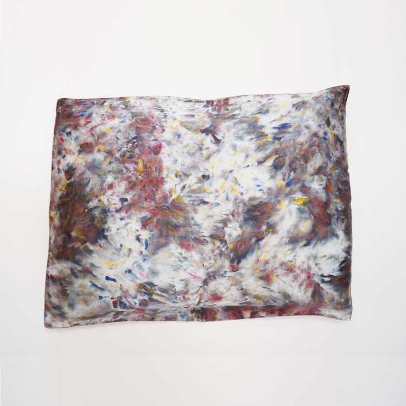 May include: A white pillowcase with a colorful abstract pattern in shades of blue, red, yellow, and brown. The pattern resembles a tie-dye design.