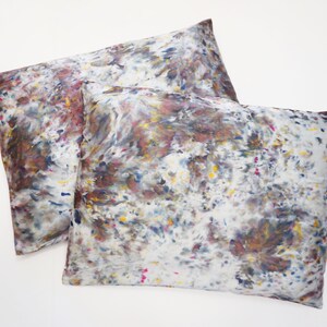 May include: Two pillowcases with a white background and a colorful abstract pattern in shades of brown, blue, yellow, and pink.