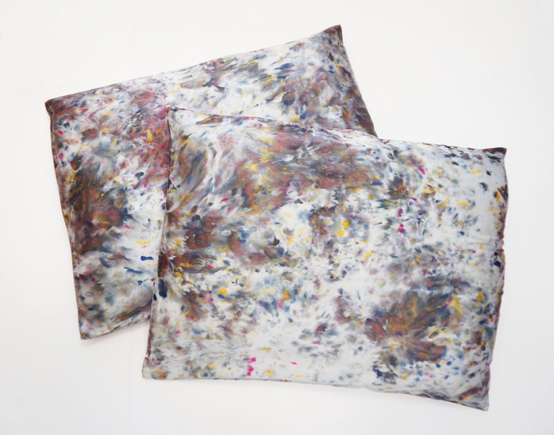 May include: Two pillowcases with a white background and a colorful abstract pattern in shades of brown, blue, yellow, and pink.