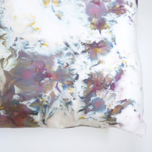 Może przedstawiać: Biała poduszka z wzorem tie-dye w odcieniach fioletu, niebieskiego, brązowego i ż&oacute;łtego.