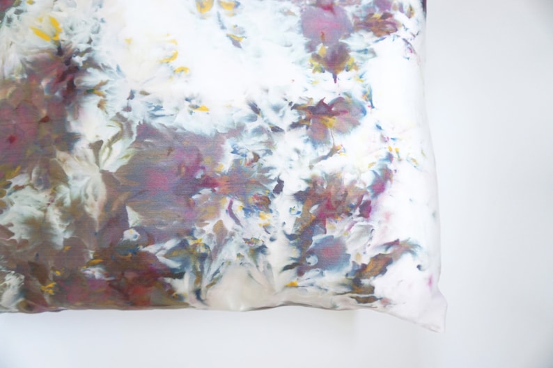 Może przedstawiać: Biała poduszka z wzorem tie-dye w odcieniach fioletu, niebieskiego, brązowego i ż&oacute;łtego.