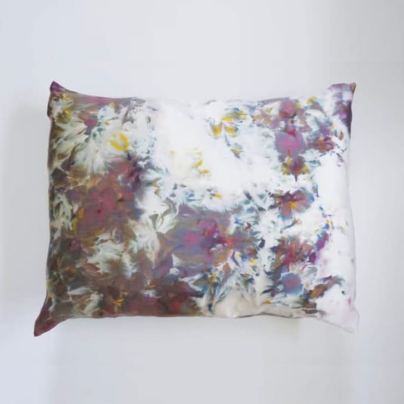 Może przedstawiać: Biała poszewka na poduszkę z wzorem tie-dye w odcieniach fioletu, brązu i błękitu. Wz&oacute;r przypomina kwiaty i liście.