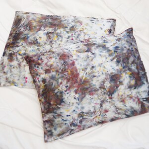 May include: Two pillowcases with a white background and a colorful abstract pattern in shades of brown, blue, yellow, and pink.
