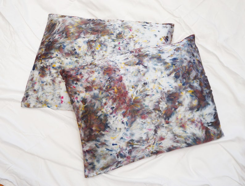 May include: Two pillowcases with a white background and a colorful abstract pattern in shades of brown, blue, yellow, and pink.