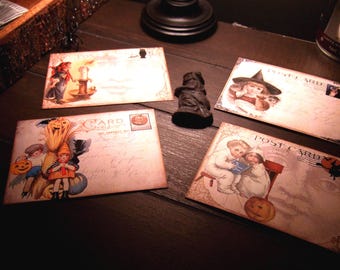 May include: Four rectangular postcards featuring vintage-style Halloween illustrations of children, pumpkins, and witches, arranged around a small dark figurine. Each card displays the word POSTCARD in the upper right corner with decorative borders.