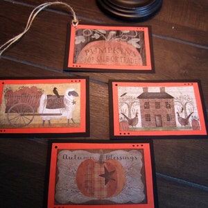 May include: Four fall-themed gift tags with black borders and orange accents. The tags feature images of a pumpkin, a house, a sheep pulling a wagon full of pumpkins, and a pumpkin with the text "Autumn Blessings".