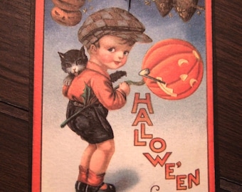 May include: Vintage Halloween card featuring a young boy with a cat on his back, holding a carved pumpkin. The card has a red border and the words "Halloween Night" are printed on the card. The background includes pumpkins and owls.