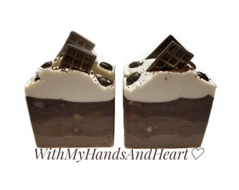 May include: Two square soaps resembling desserts, with layers of brown and white, topped with chocolate squares and coffee beans. The soaps have the text "WithMyHandsAndHeart" on the bottom.