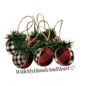 May include: A set of five spherical ornaments covered in red, black, and white buffalo plaid fabric. Each ornament features a small cluster of green artificial pine needles at the top and a brown twine loop for hanging. The text WithMyHandsAndHeart is visible.