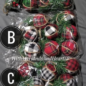 May include: Three clear plastic bags containing round fabric-covered ornaments with plaid patterns in red, green, black, and white. Each ornament is accented with green artificial pine needles, small red berries, and a jute twine hanging loop.
