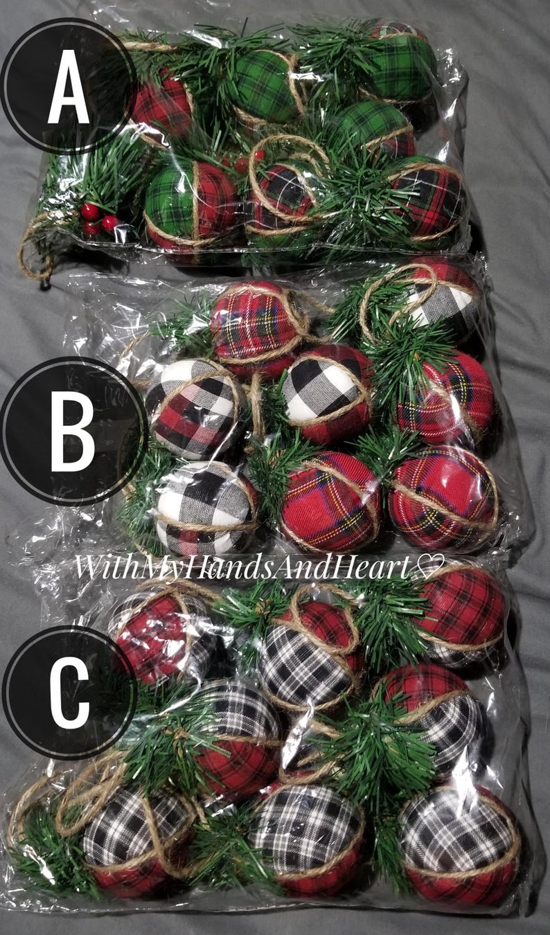 May include: Three clear plastic bags containing round fabric-covered ornaments with plaid patterns in red, green, black, and white. Each ornament is accented with green artificial pine needles, small red berries, and a jute twine hanging loop.