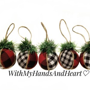 May include: Five spherical ornaments wrapped in red and black buffalo plaid fabric, each topped with a small cluster of green pine needles and a jute twine hanging loop. The text WithMyHandsAndHeart is printed below the ornaments.