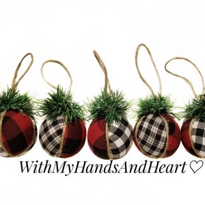 May include: Five spherical ornaments wrapped in red and black buffalo plaid fabric, each topped with a small cluster of green pine needles and a jute twine hanging loop. The text WithMyHandsAndHeart is printed below the ornaments.