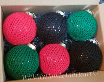 May include: A set of six spherical ornaments in a cardboard box, each wrapped in a knitted cover. The collection includes two red, two black, and two green ornaments, all featuring a metallic silver cap at the top for hanging purposes.