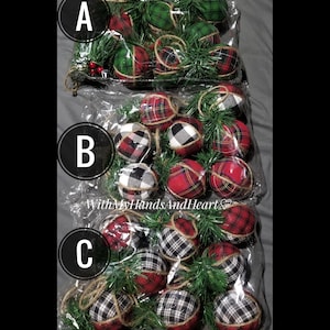 May include: Three clear plastic bags labeled A, B, and C, each containing multiple fabric-covered spherical ornaments. The ornaments feature red, green, black, and white plaid or buffalo check patterns, accented with green pine sprigs and twine.