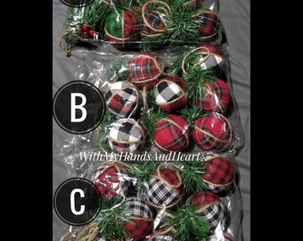 May include: Three clear plastic bags labeled A, B, and C, each containing multiple fabric-covered spherical ornaments. The ornaments feature red, green, black, and white plaid or buffalo check patterns, accented with green pine sprigs and twine.