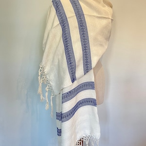May include: White prayer shawl with blue stripes and fringe. The shawl is made of a soft, woven fabric and has a traditional design.