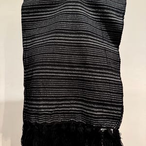 May include: A black and white striped scarf with a fringe trim. The scarf features horizontal stripes in varying widths, with a prominent fringe along the bottom edge. The fabric appears to be woven, creating a textured look.