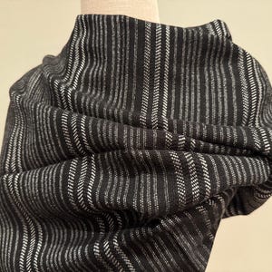 May include: A black and white striped scarf draped over a mannequin. The scarf has a vertical stripe pattern with alternating black and white lines. The fabric appears to be soft and textured, with a slight sheen.