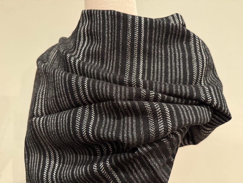 May include: A black and white striped scarf draped over a mannequin. The scarf has a vertical stripe pattern with alternating black and white lines. The fabric appears to be soft and textured, with a slight sheen.